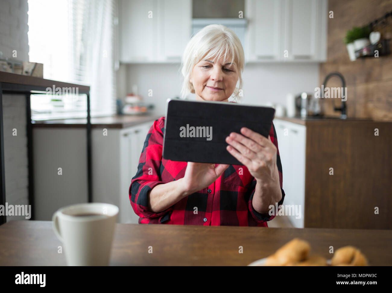 Ritratto di signora senior utilizzando tablet al tavolo della cucina Foto Stock