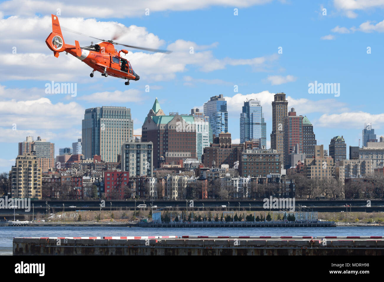 Un Coast Guard MH-65 Dolphin decolla dal centro di Manhattan eliporto nella città di New York il 24 marzo 2018. Lo skyline del centro cittadino di Brooklyn, uno di New York City in cinque boroughs, può essere visto in background. (U.S. Coast Guard foto di Sottufficiali di terza classe Steve Strohmaier) Foto Stock