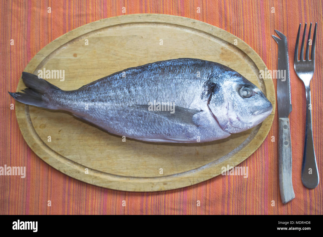 Fresh orata pesce sul piatto di legno con vicino a forchetta e coltello Foto Stock