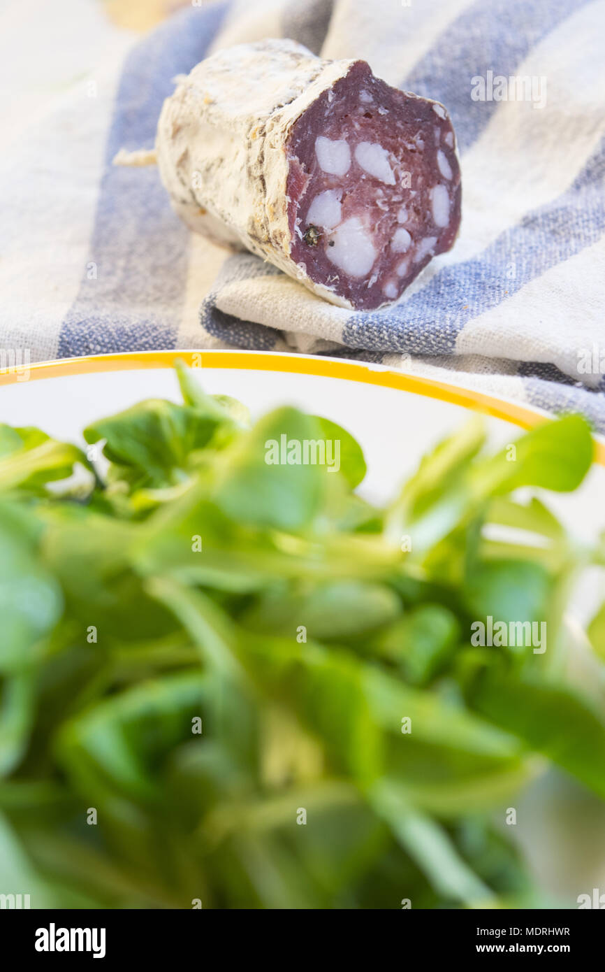 Pezzo di salame salsiccia affumicata in prossimità di una fresca insalata di lattuga Foto Stock