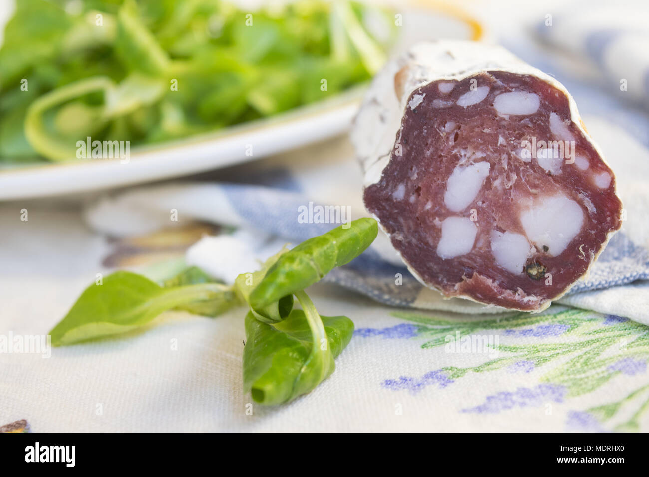 Pezzo di salame salsiccia affumicata in prossimità di una fresca insalata di lattuga Foto Stock