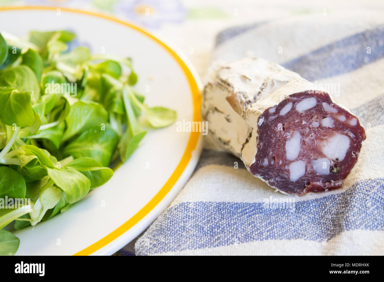 Pezzo di salame salsiccia affumicata in prossimità di una fresca insalata di lattuga Foto Stock