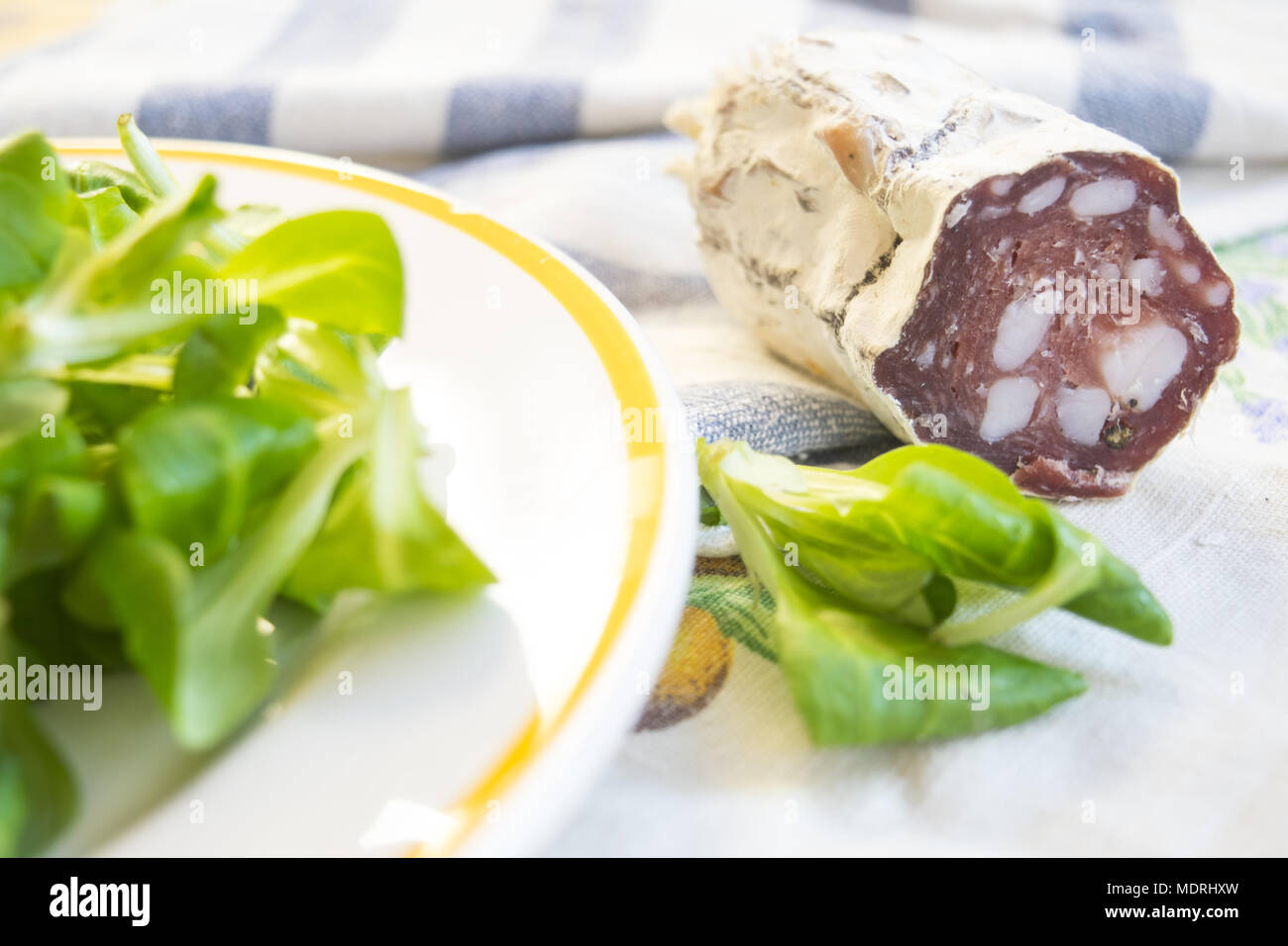 Pezzo di salame salsiccia affumicata in prossimità di una fresca insalata di lattuga Foto Stock