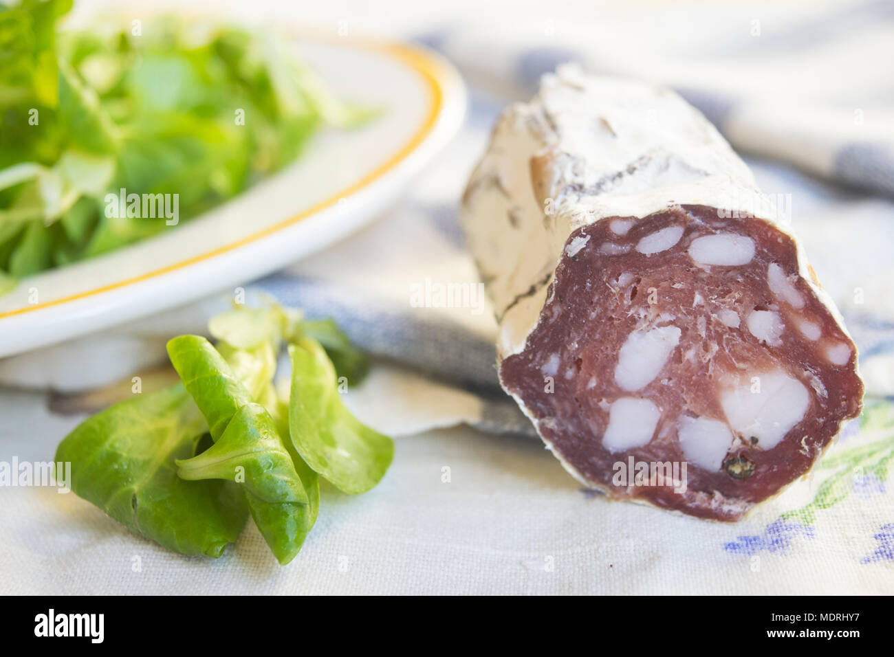 Pezzo di salame salsiccia affumicata in prossimità di una fresca insalata di lattuga Foto Stock