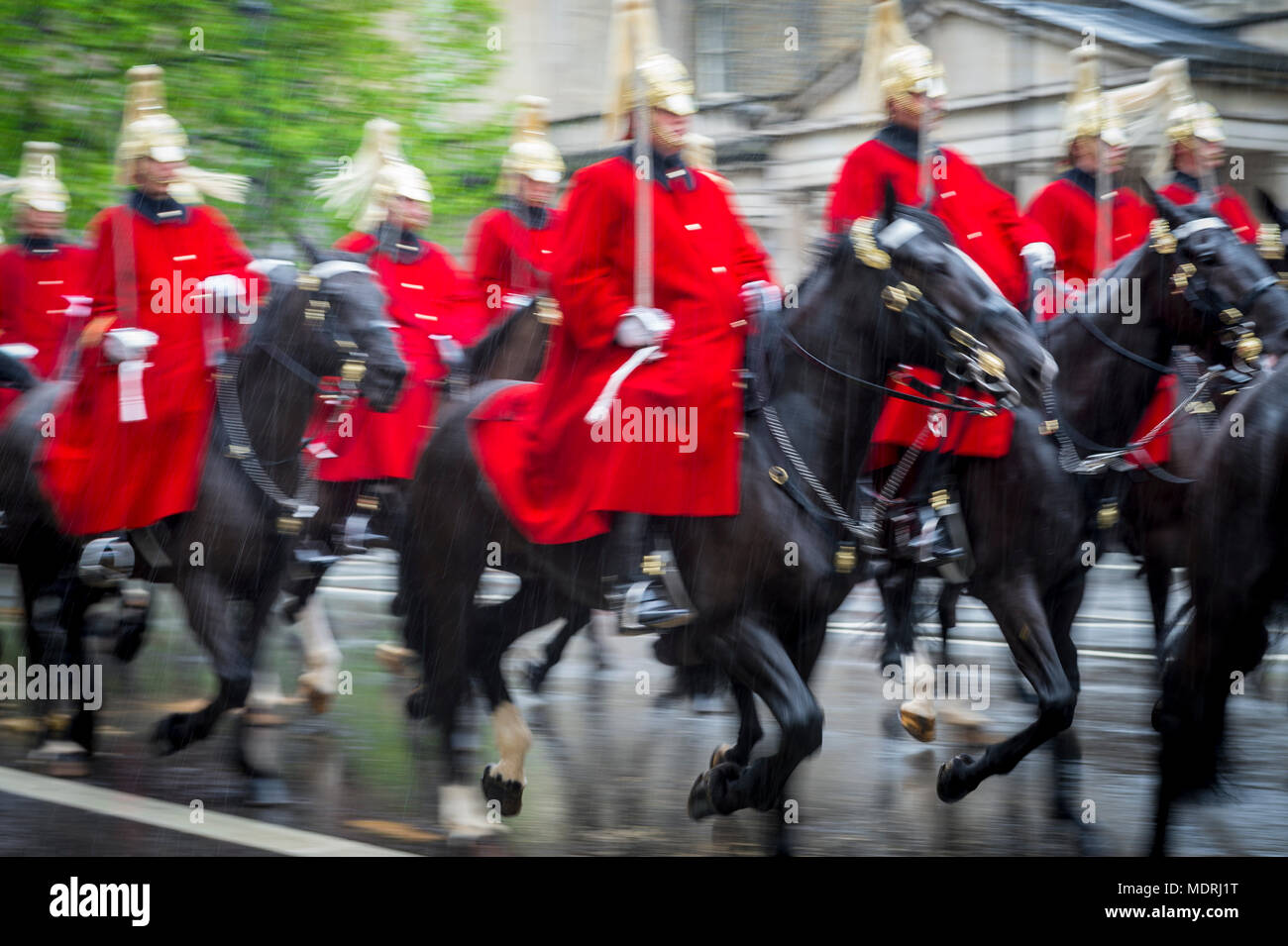 Guardia Reale a cavallo vestiti di rosso cerimoniale cappotti passano con motion blur in una sfilata in un giorno di pioggia a Londra, Inghilterra, Regno Unito. Girato con chiusura lento Foto Stock