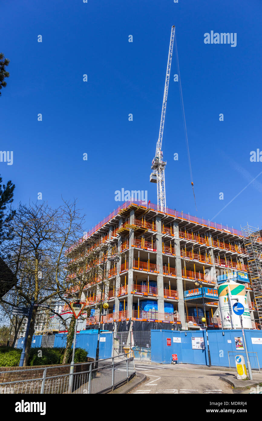 Guscio di un nuovo appartamento residenziale blocco in costruzione vicino alla stazione ferroviaria e la torre bianca gru, Woking, Surrey, Regno Unito in una giornata di sole Foto Stock