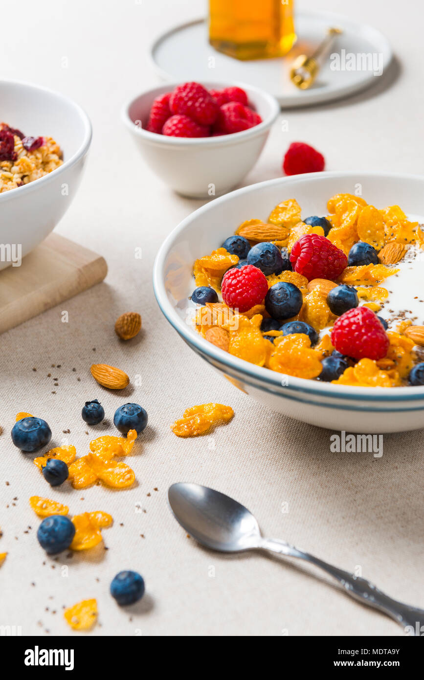 Una sana prima colazione. Fiocchi di mais con yogurt, mandorle, mirtilli e lamponi e semi di Chia. Servite con lo sciroppo di acero e succo di frutta sulla tela beige. Foto Stock