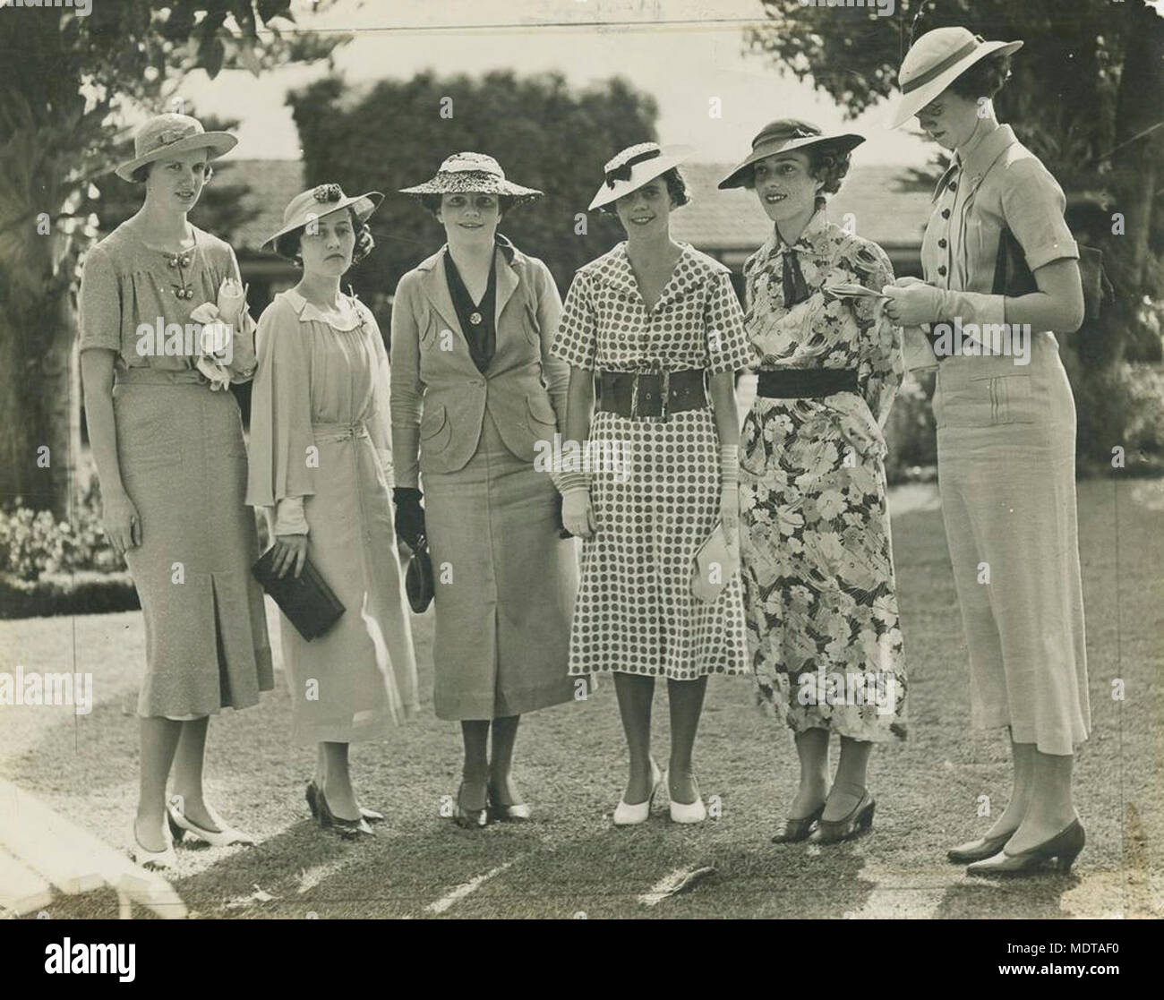 Gruppo di donne godendo una giornata di gare,. Posizione: Brisbane, Queensland, Australia Data: Senza Data Descrizione: sei signore, tutti indossano abiti smart e largo-colmato cappelli, sono riuniti sul prato alle gare. Foto Stock