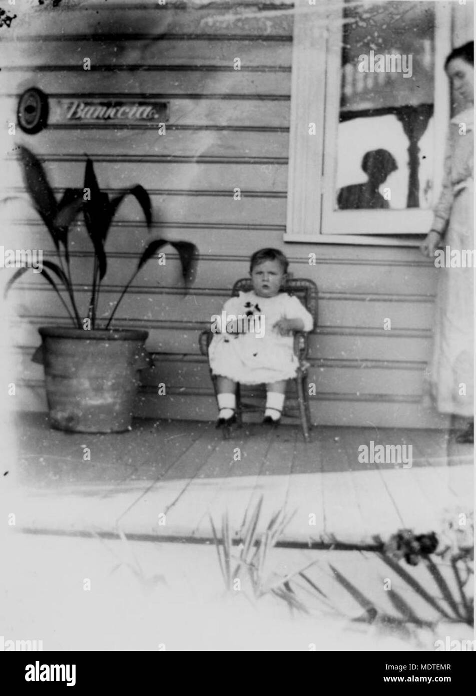 Bambino in una piccola sedia di canna su una veranda. Foto Stock