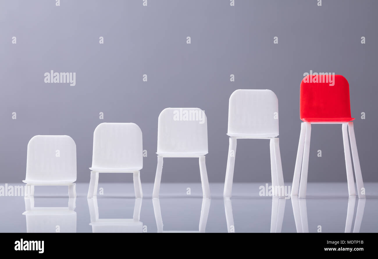 Scala crescente di svuotare il bianco e il rosso delle sedie in fila contro lo sfondo grigio Foto Stock