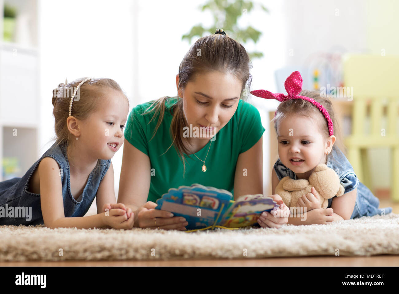 La famiglia felice con bambini leggere una storia la posa sul pavimento in camera dei ragazzi Foto Stock