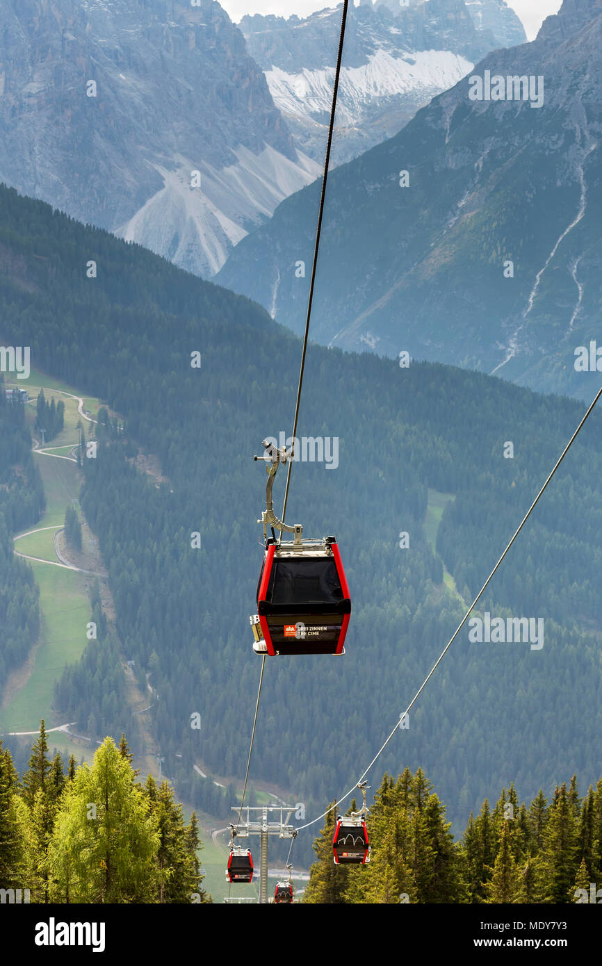 Cabine in gondola lungo il cavo con ripide piste alpine e le montagne in distanza; Sesto, Bolzano, Italia Foto Stock