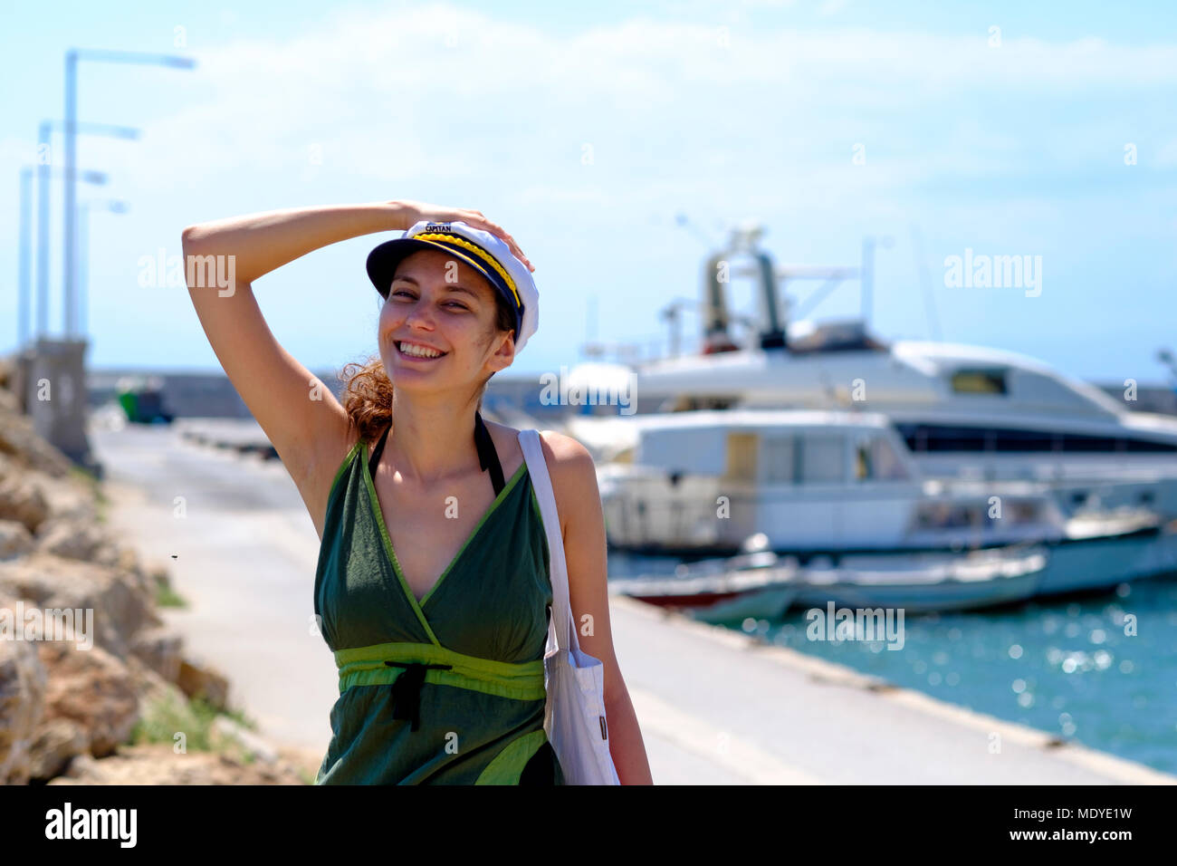 Giovane bella ragazza in un abito verde con un capitano hat su un molo vicino a uno yacht Foto Stock