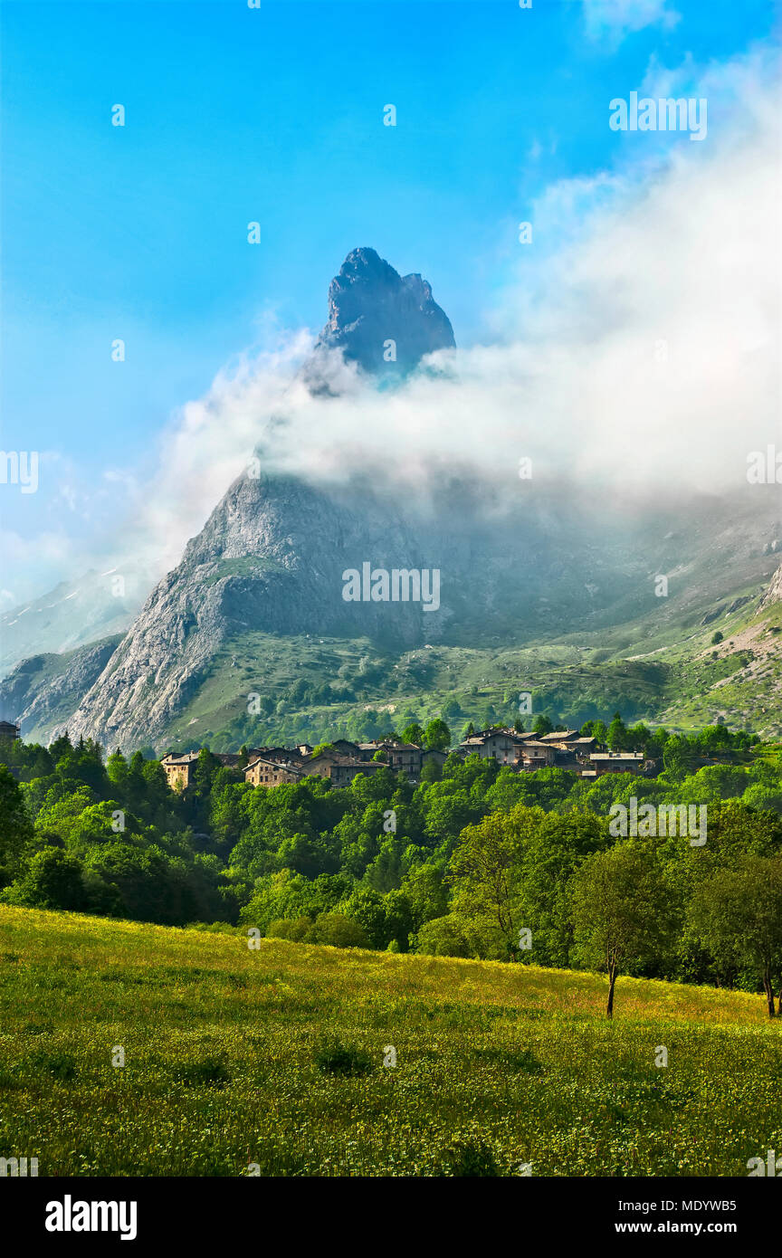 Il villaggio di Chiappera, nella parte superiore della Valle Maira in Piemonte, surmonted dal Provenzale Rock, parzialmente avvolto dalle nuvole. Foto Stock