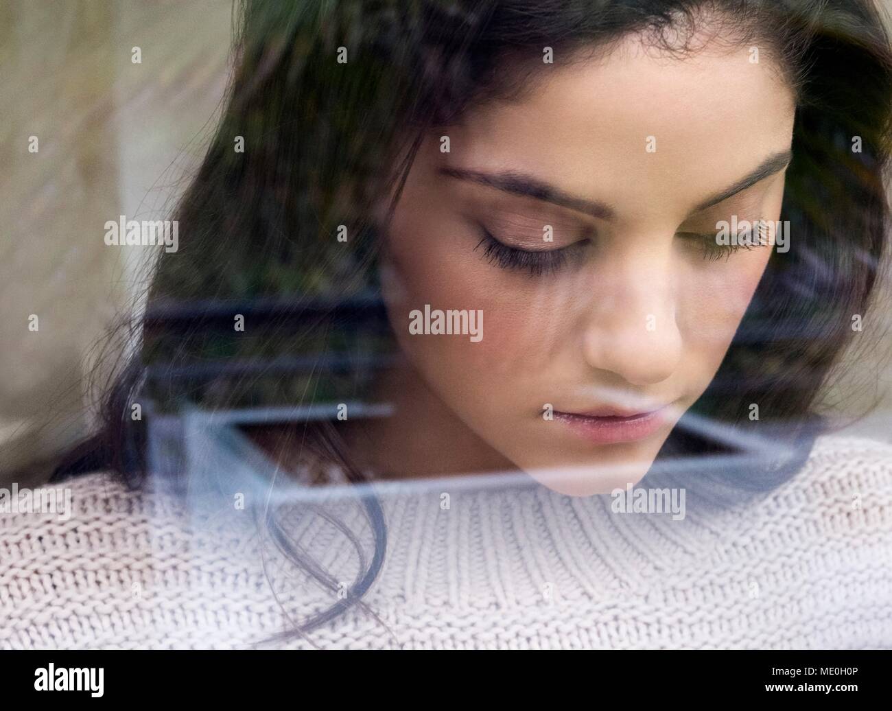 Giovane donna che guarda verso il basso, vista attraverso il vetro riflettente. Foto Stock