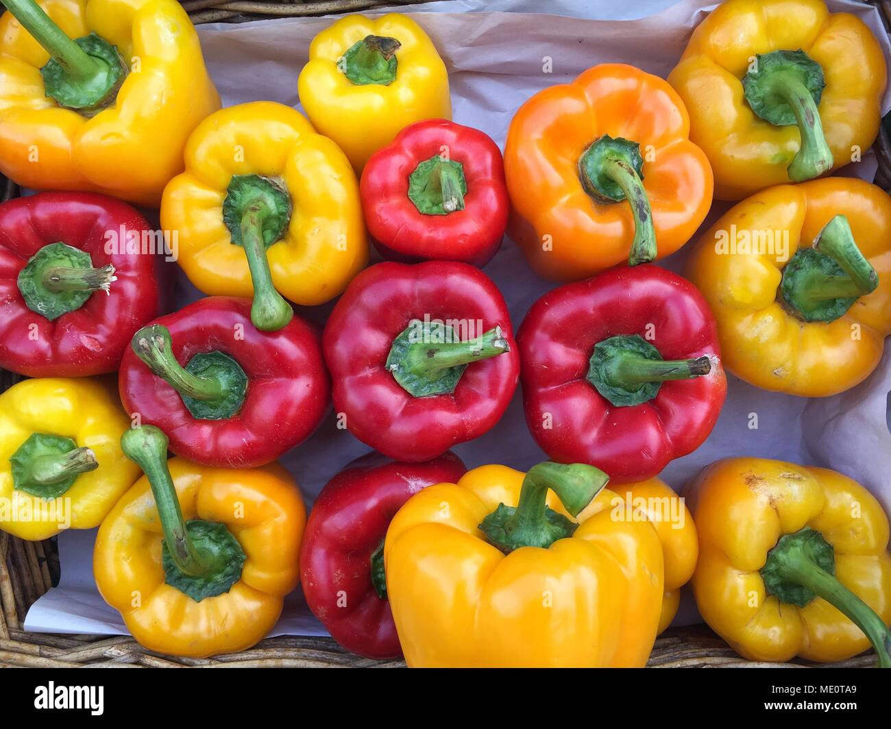 Un cesto pieno di colorati peperoni in giallo, rosso e arancio in un mercato all'aperto in stallo Foto Stock