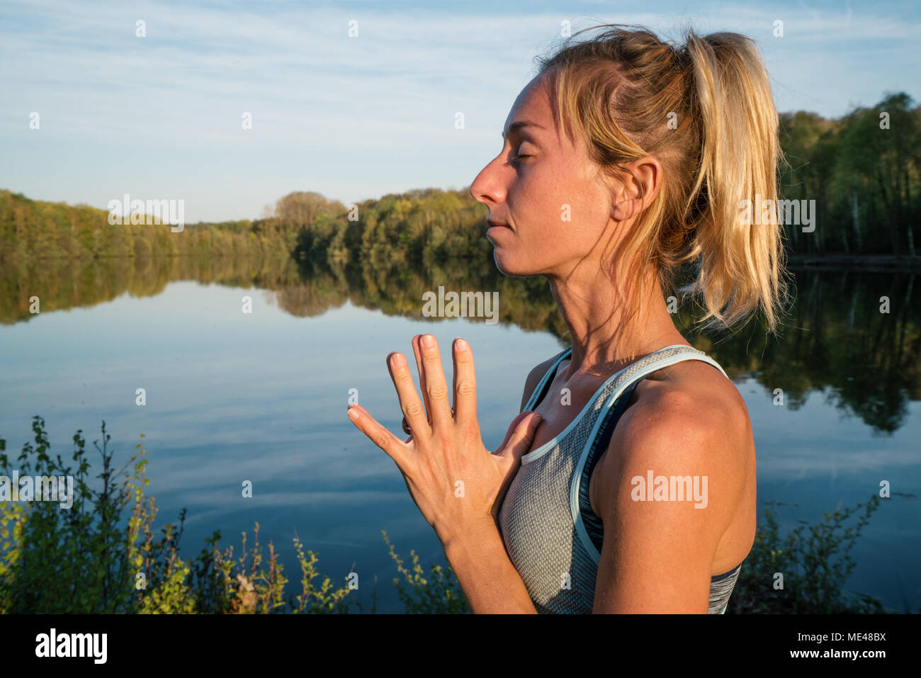 Giovane donna esercizio di yoga in riva al lago al tramonto, persone Viaggi natura benessere e relax concetto. Girato in Francia, l'Europa. Mani al cuore Foto Stock