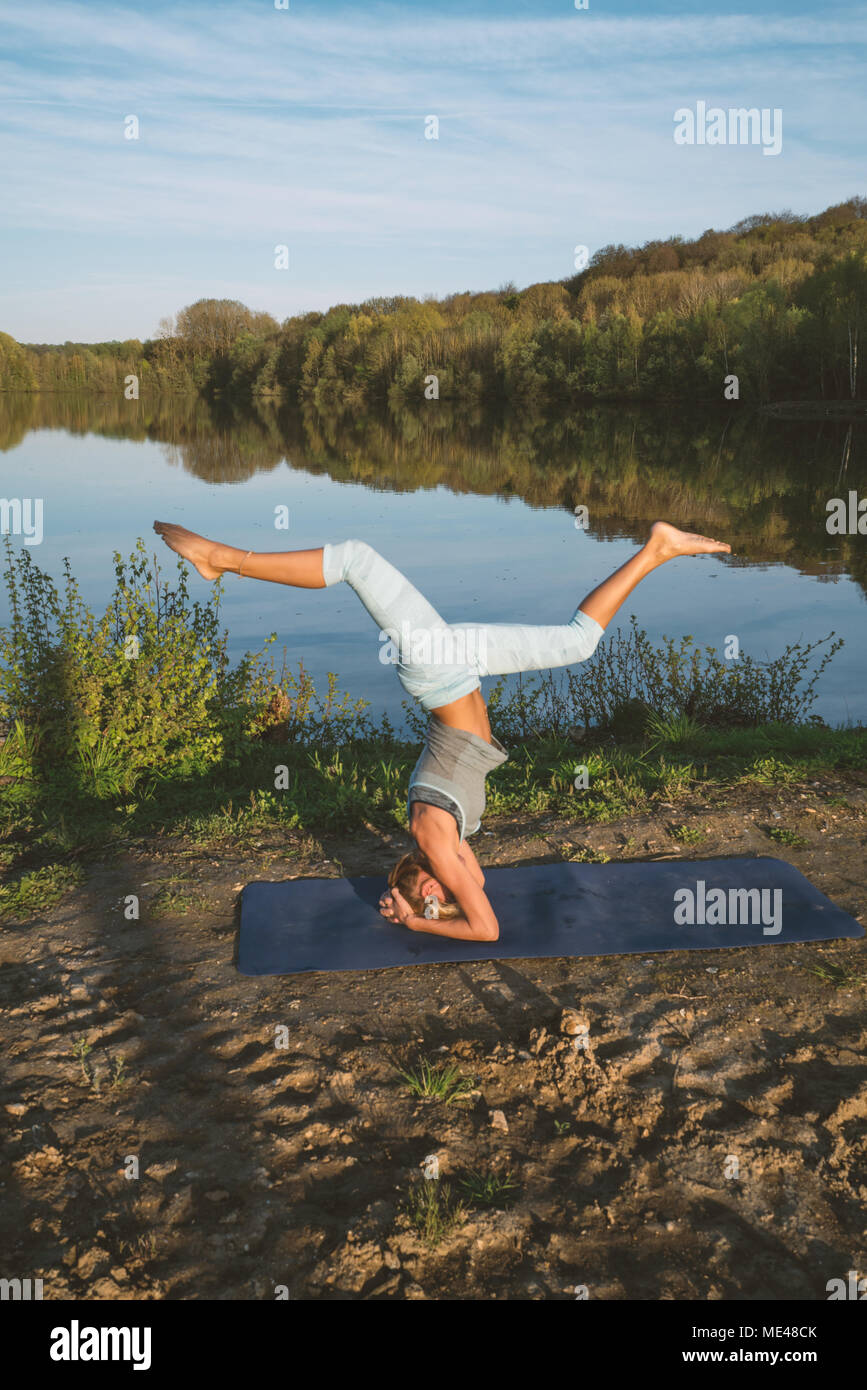Giovane donna esercizio di yoga in riva al lago al tramonto, persone Viaggi natura benessere e relax concetto. Girato in Francia, l'Europa. HEADSTAND Foto Stock