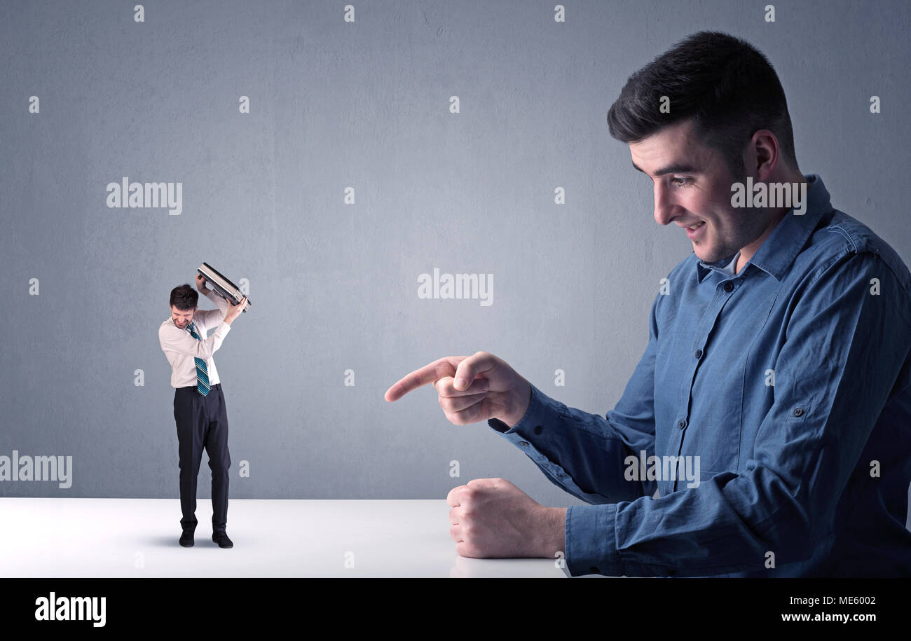 Giovane imprenditore professionale essendo arrabbiato con un altro imprenditore in miniatura nella parte anteriore di un bluastro sfondo grigio Foto Stock