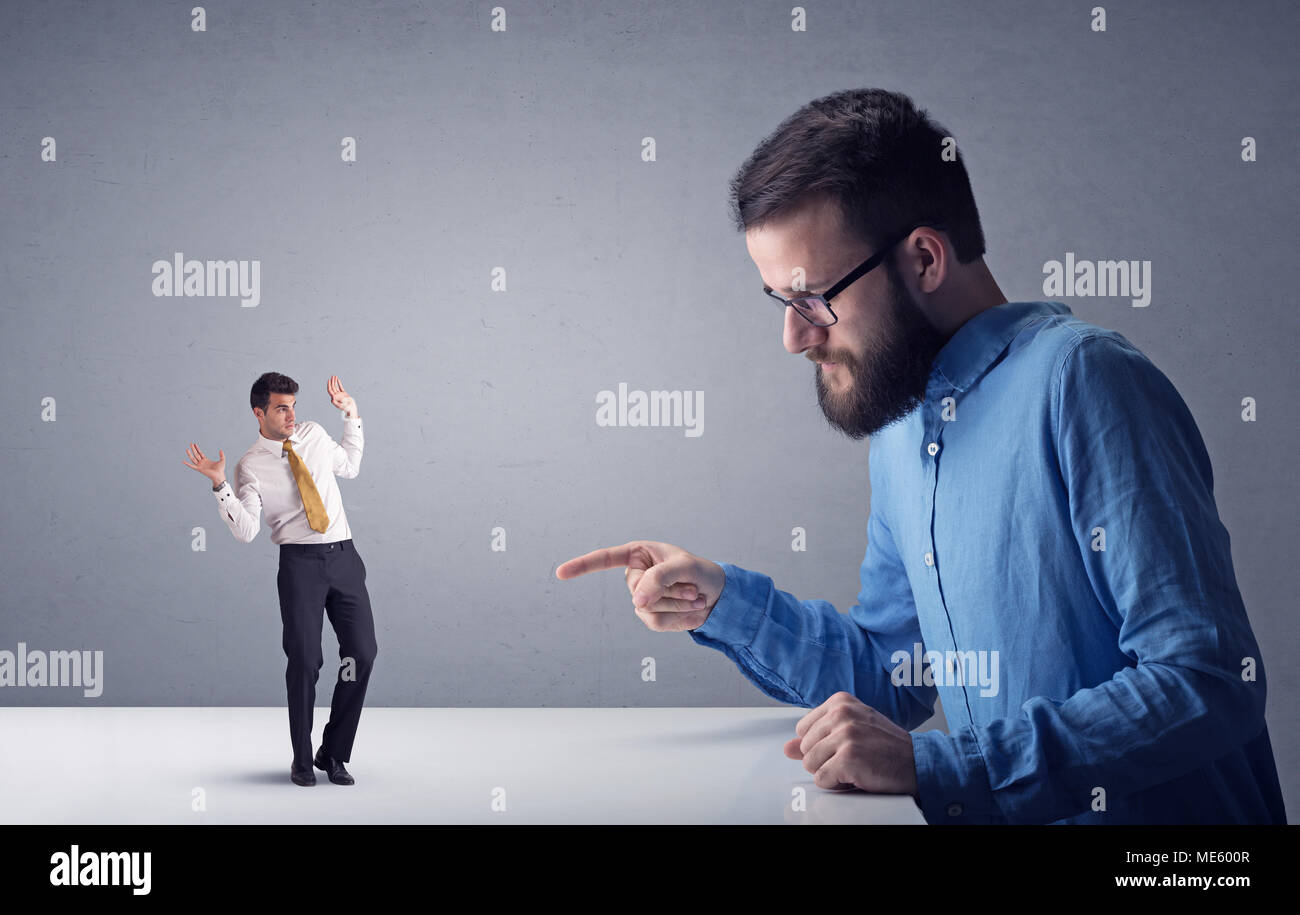 Giovane imprenditore professionale essendo arrabbiato con un altro imprenditore in miniatura di fronte a uno sfondo grigio Foto Stock
