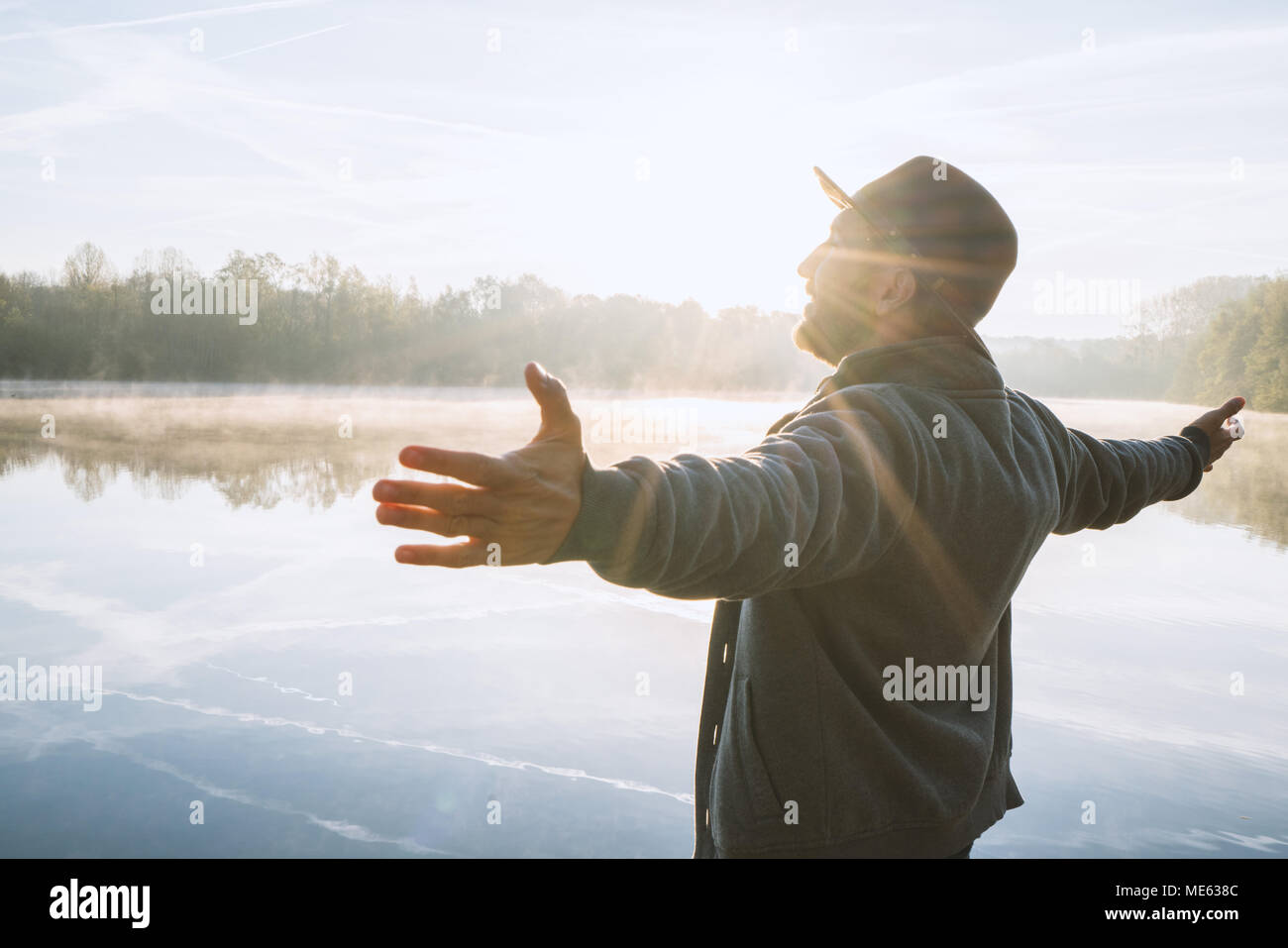 Giovane uomo braccia tese dal lago a sunrise godendo la libertà e la vita, persone viaggi benessere concetto. Girato in Francia, l'Europa. Foto Stock