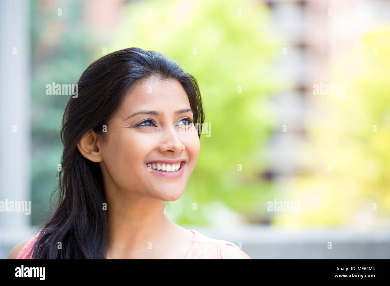 Closeup ritratto headshot, sorridente, gioioso, felice giovane donna che guarda verso l'alto fantasticando cose belle, isolata all'esterno soleggiato, costruzione di sfondo. P Foto Stock