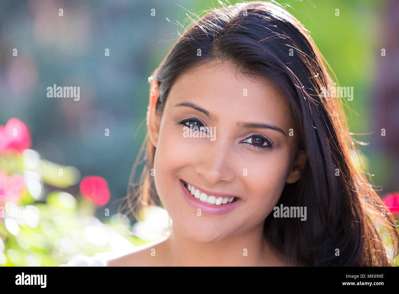 Closeup headshot ritratto di fiducioso sorridendo felice piuttosto giovane donna, isolato di sfondo sfocato alberi, fiori. Umani positivi del viso emozione Foto Stock