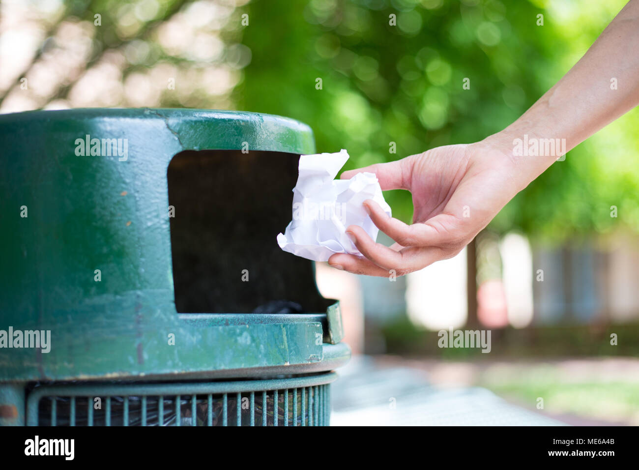 Primo piano ritagliato ritratto di qualcuno tossing accartocciata pezzo di carta nel cestino, isolata all'esterno verdi alberi sullo sfondo Foto Stock