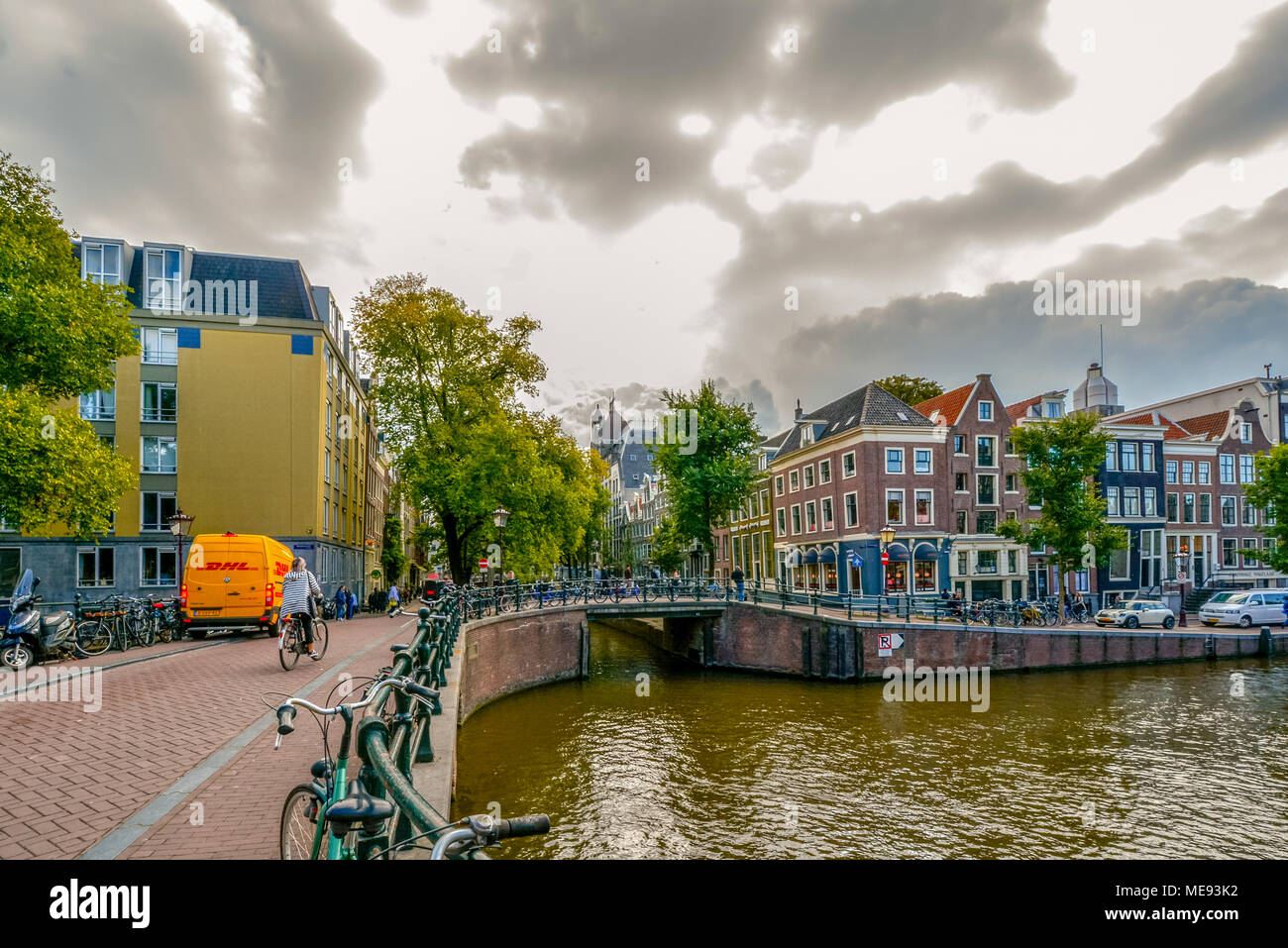Una donna Olandese cavalca il suo moto attraverso un ponte su un canale su un nuvoloso giorno di autunno in Amsterdam Paesi Bassi Foto Stock