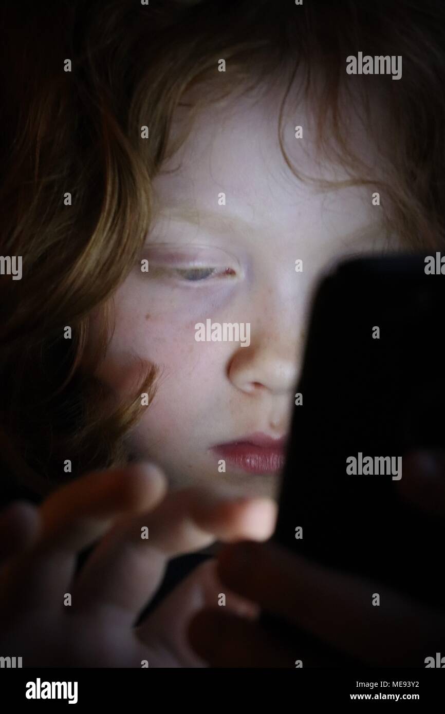Una giovane ragazza con i capelli di zenzero utilizza un Touch Screen Mobile Phone per giocare Foto Stock