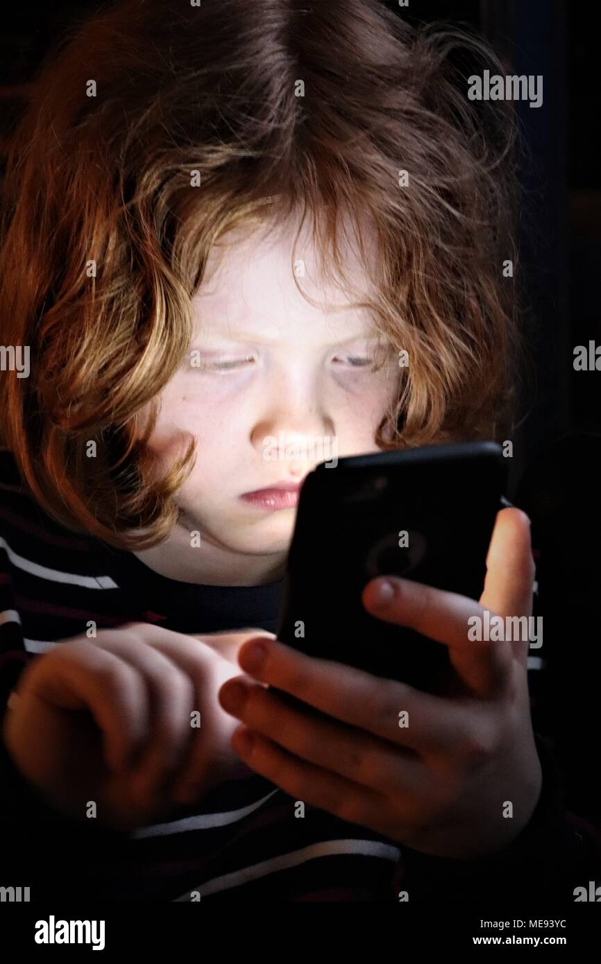 Una giovane ragazza con i capelli di zenzero utilizza un Touch Screen Mobile Phone per giocare Foto Stock