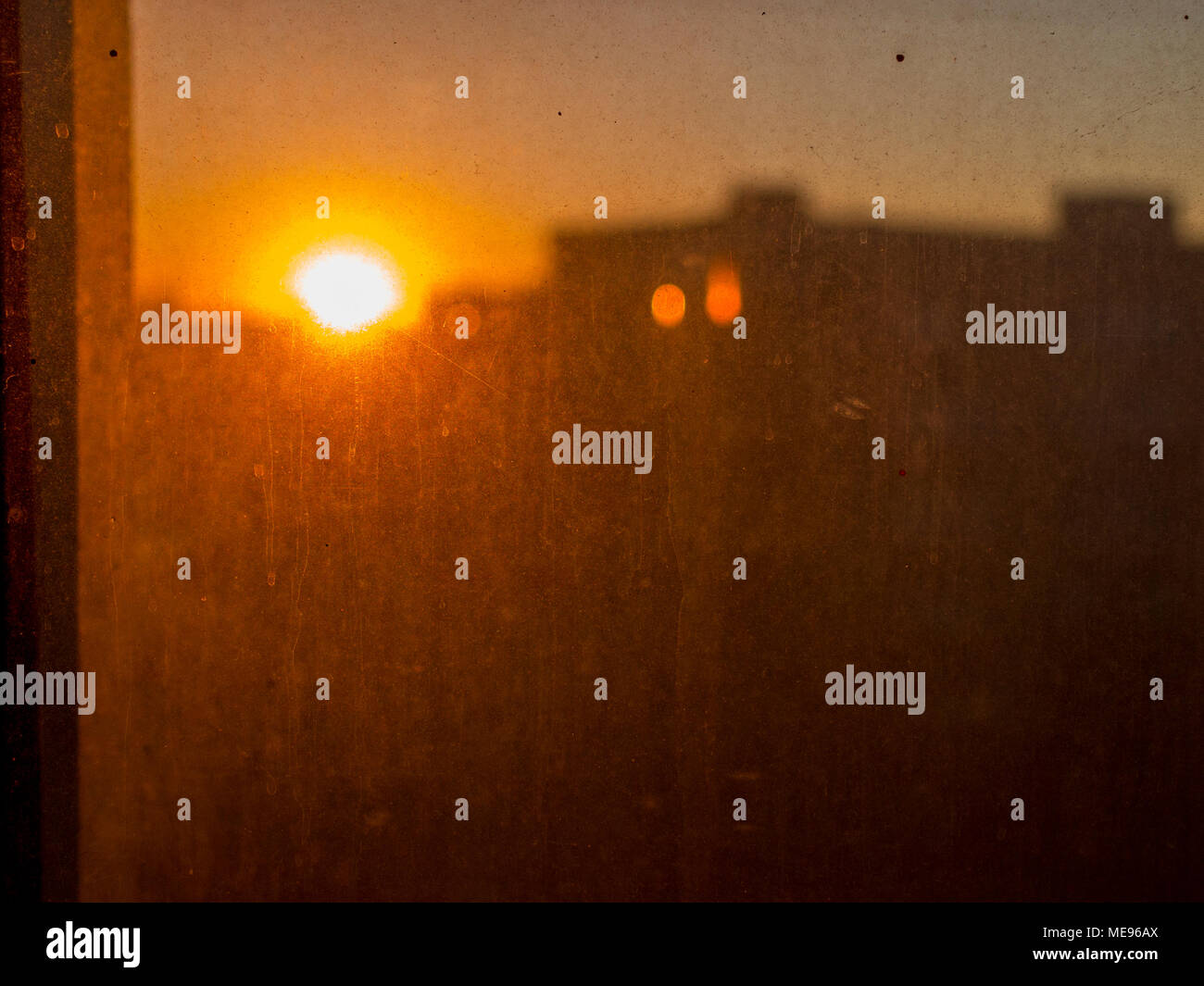Vista del tramonto rosso dietro molto polveroso e vetro sporco nella città Foto Stock