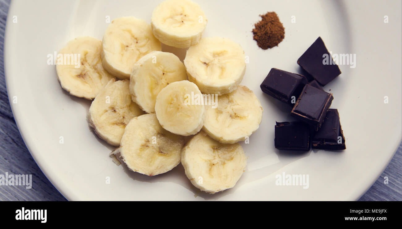 Il cioccolato fondente, banana e cannella. Ingredienti per un smoothie sulla piastra bianca. Vista superiore foto. Foto Stock