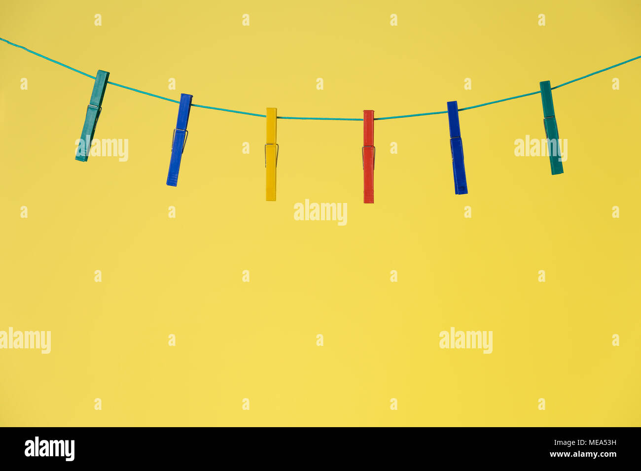 Clothespins colorati sulla corda isolato su sfondo giallo Foto Stock