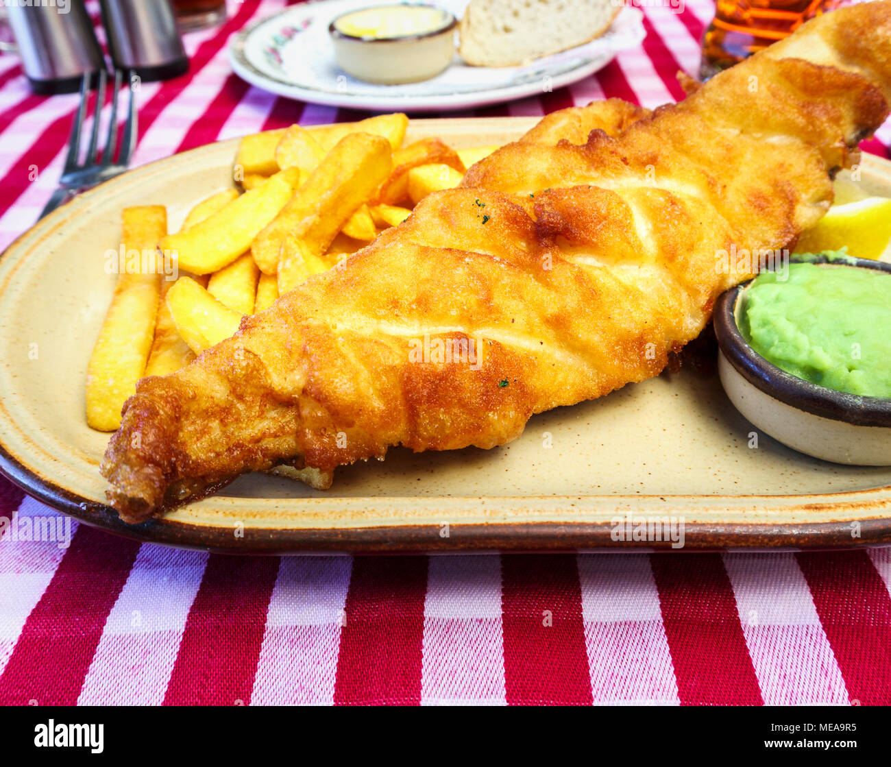 Bistrattato pesce (birra pastella), golden chips, fiacco piselli il pranzo o la cena: piastra di pub inglese tradizionale cibo su un bianco e rosso Gingham controllare la tovaglia Foto Stock