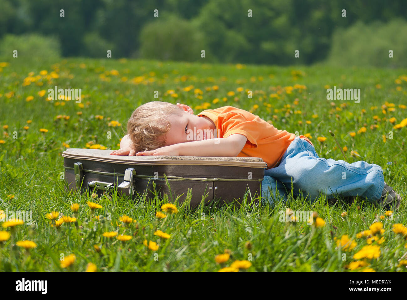 Ritratto di carino sorridente volto felice di adorabile bambino bianco recante su marrone vintage valigia outdoor sulla molla luminosa giornata di sole. Orizzontale foto a colori Foto Stock