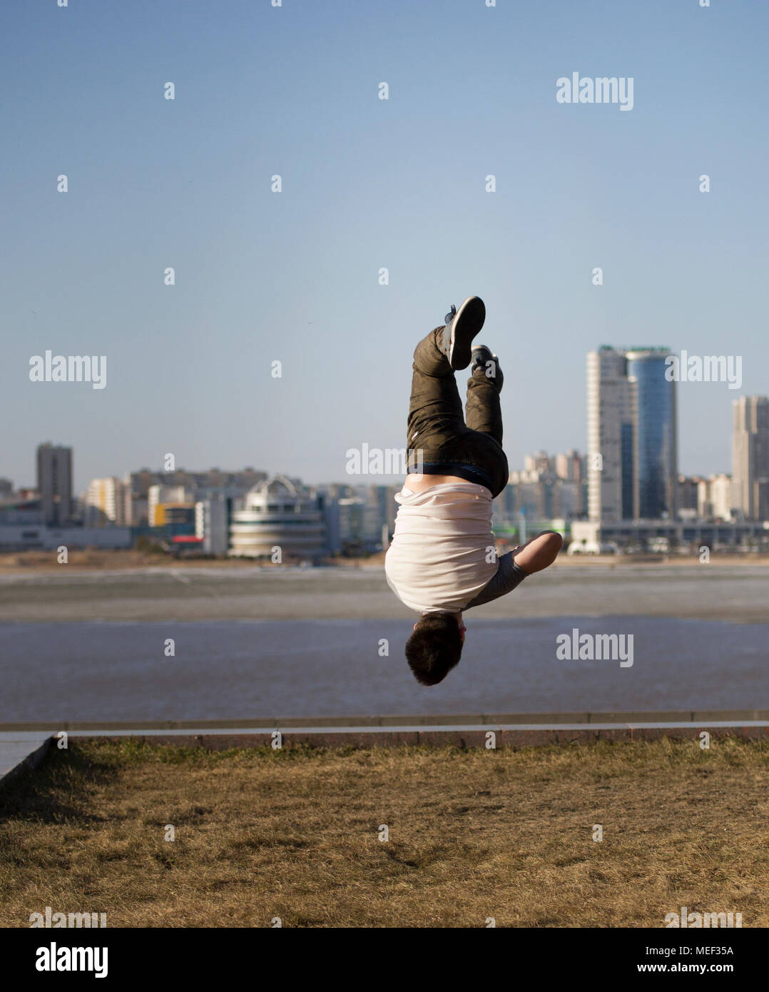Giovane maschio sportivo acrobatico esegue trucchi capovolto nella parte anteriore della skyline Foto Stock