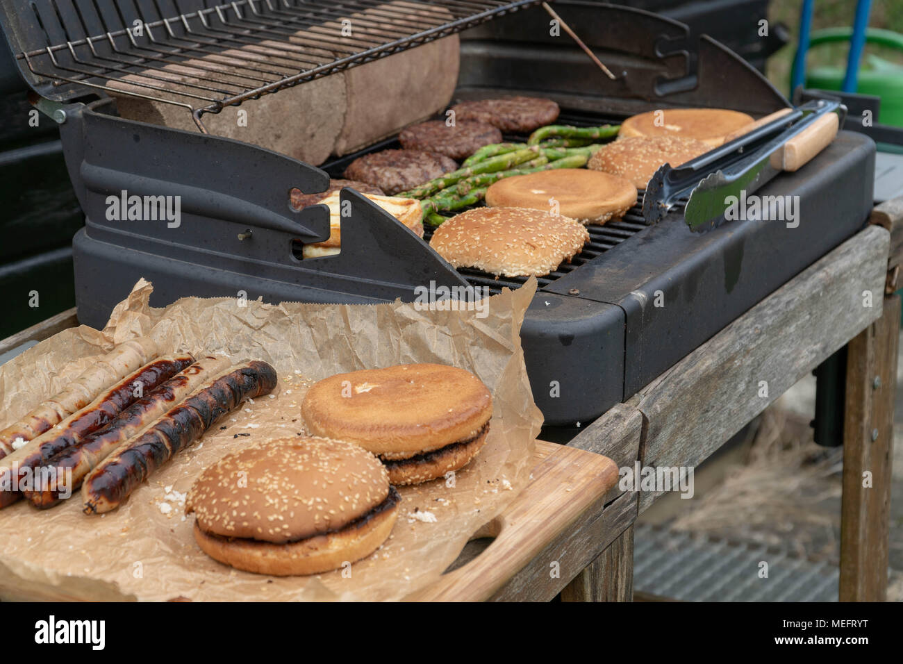 Set di hamburger. La persona che sta andando a griglia polpette di carne, salsicce, formaggio alla griglia e asparagi Foto Stock
