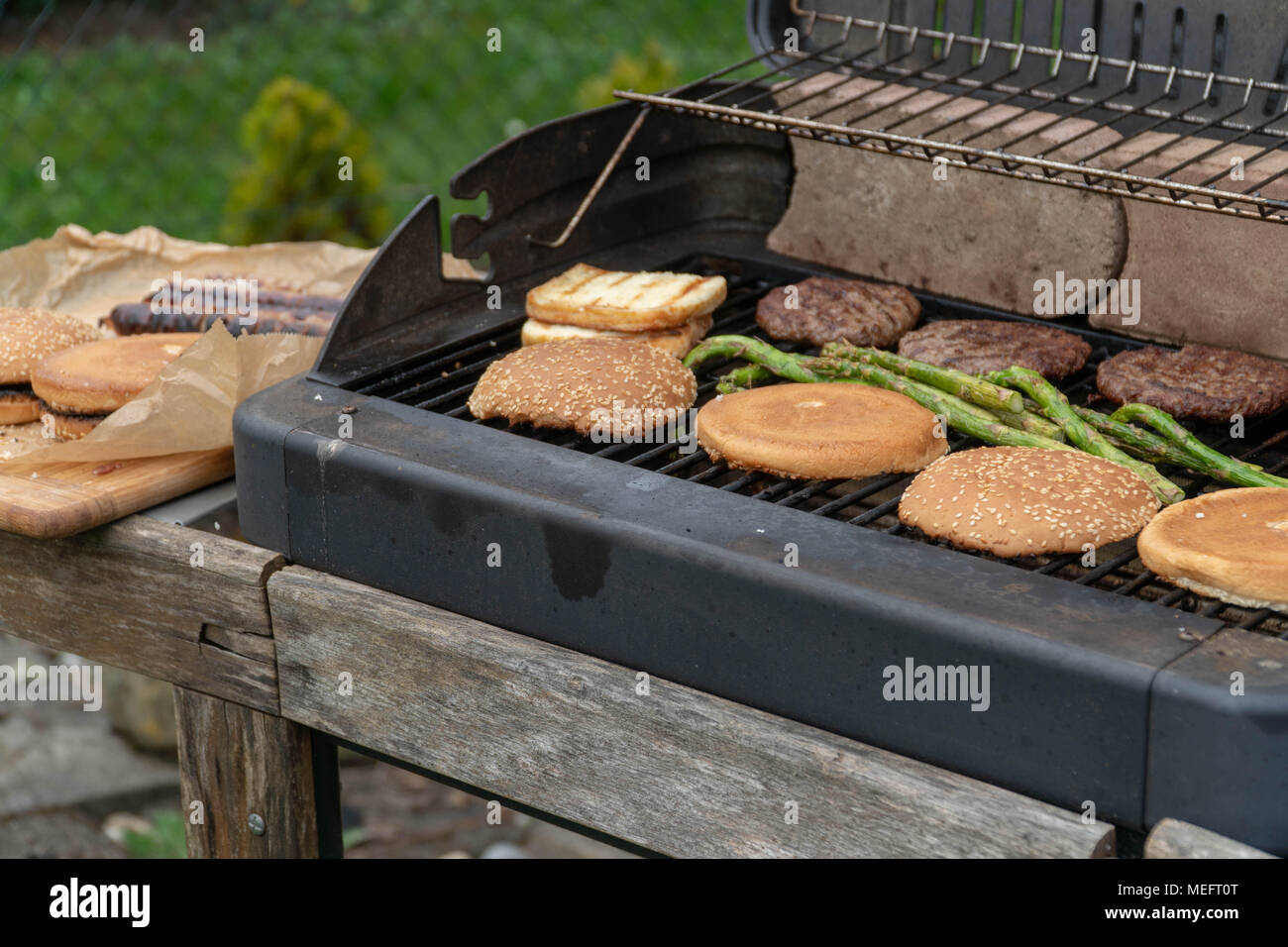 Set di hamburger. La persona che sta andando a griglia polpette di carne, salsicce, formaggio alla griglia e asparagi Foto Stock