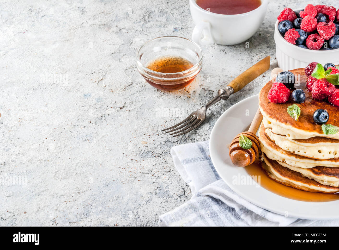 Una sana prima colazione estate,in casa classic american pancake con bacche fresche e miele, mattina pietra grigio chiaro sfondo spazio di copia Foto Stock