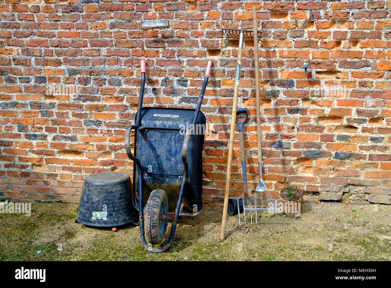 Tradizionali utensili da giardinaggio carriola due rastrelli a forcella e una plastica flexi vasca da un vecchio muro di mattoni in Helmsley Walled Garden North Yorkshire Foto Stock