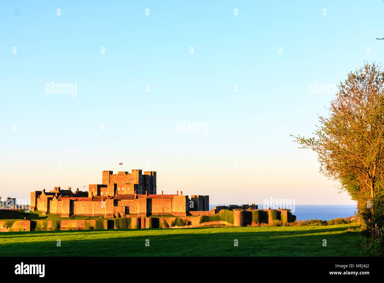 Inghilterra, il castello di Dover. Illuminato dal sole nascente (invisibile), esterno, pareti interne e di mantenere con la Manica in background. Ora d'oro cast colore all'immagine. Foto Stock