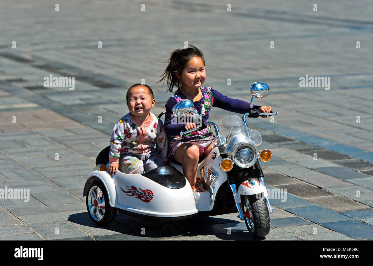 Da 6 a 8 anno vecchia ragazza a cavallo di un giocattolo elettrico motore-bike con suo fratello su Sukhbaatar Square, Ulaanbaatar, in Mongolia Foto Stock
