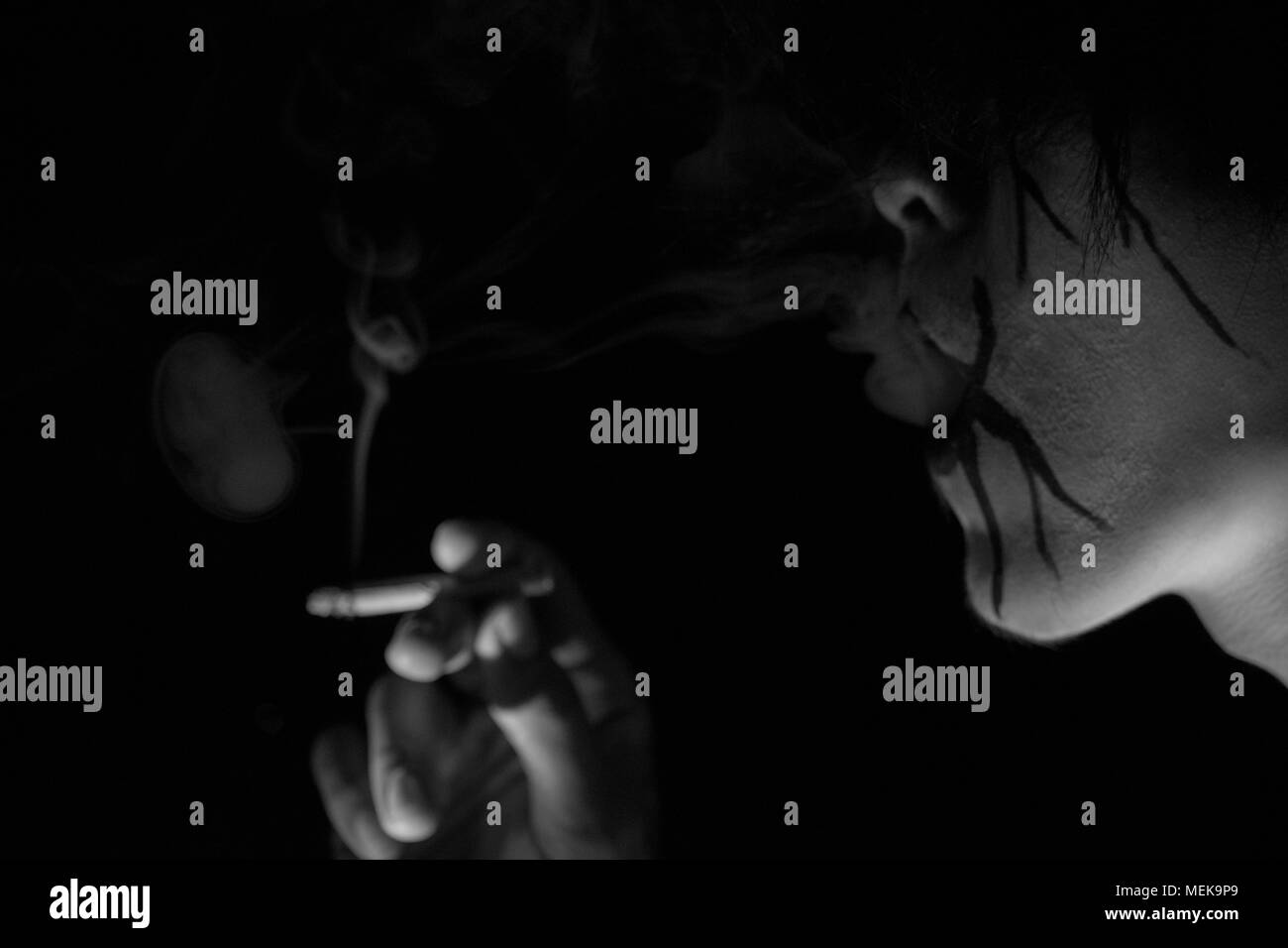 Uomo con la pittura del viso è stato il fumo con uno scuro su sfondo nero Foto Stock