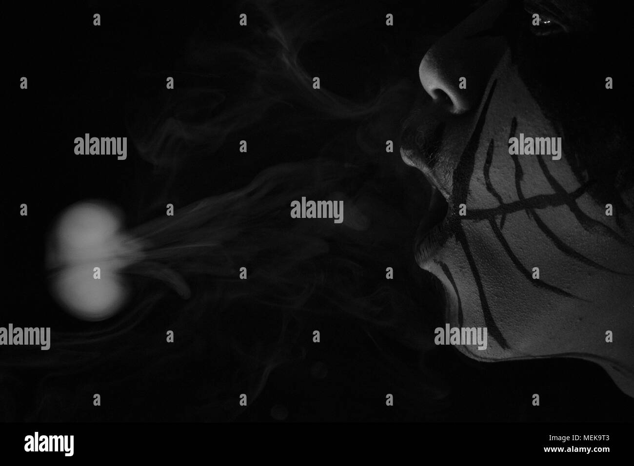 Uomo con la pittura del viso è stato il fumo con uno scuro su sfondo nero Foto Stock