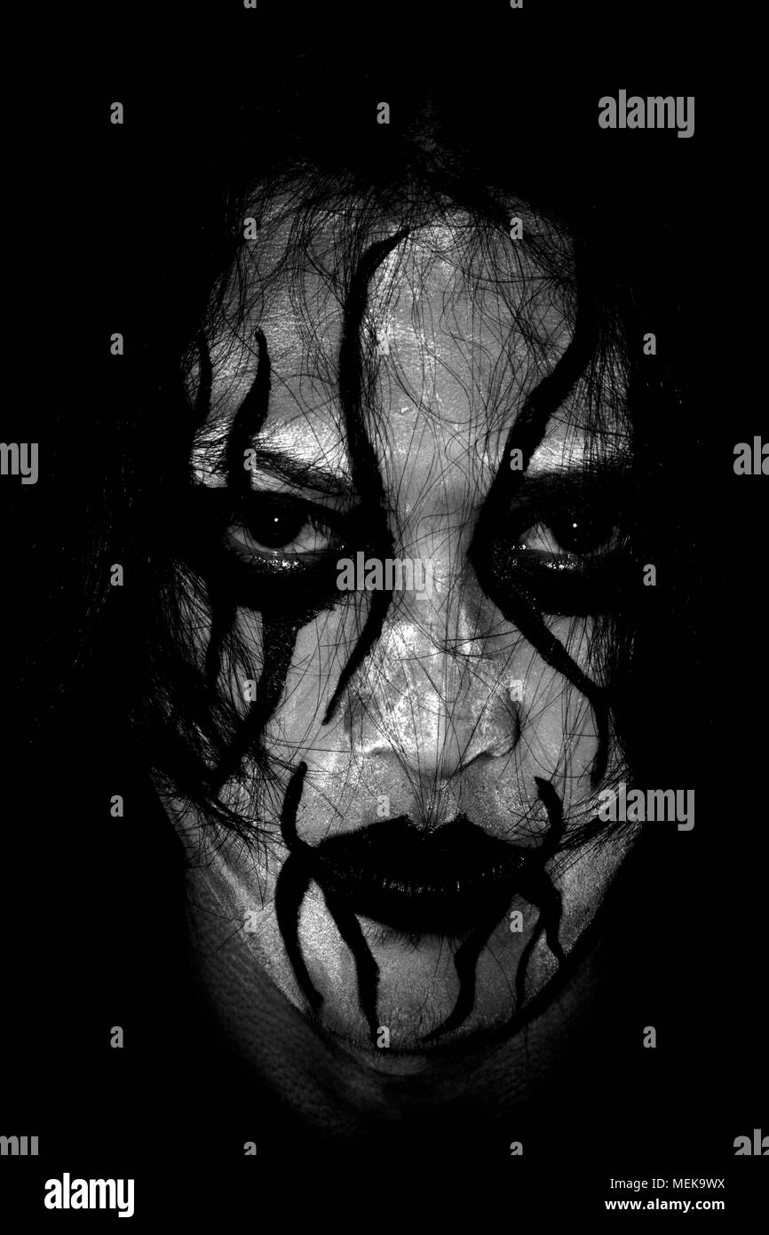 Uomo con la pittura del viso è stato il fumo con uno scuro su sfondo nero Foto Stock