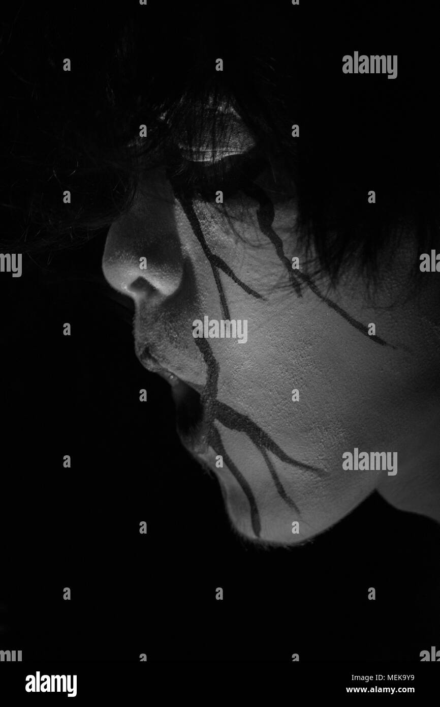 Uomo con la pittura del viso è stato il fumo con uno scuro su sfondo nero Foto Stock