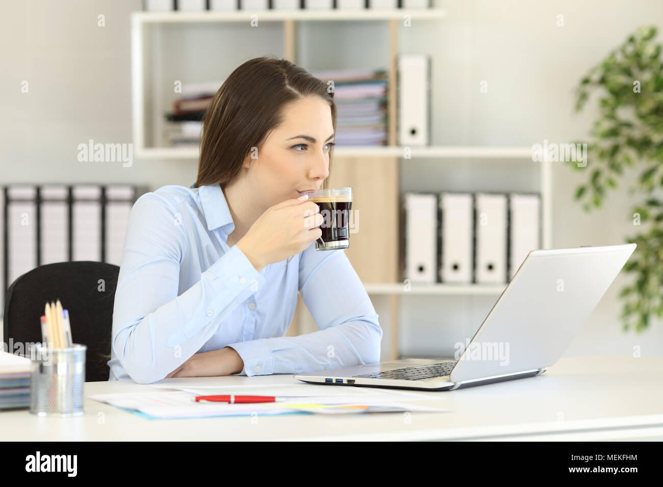 Rilassata lavoratore di ufficio avente una pausa caffè guardando il lato seduta in un desktop al lavoro Foto Stock