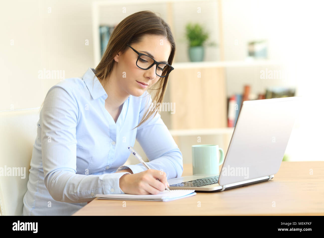 Seri lavoratori autonomi prendendo appunti su un portatile su un tavolo a casa Foto Stock