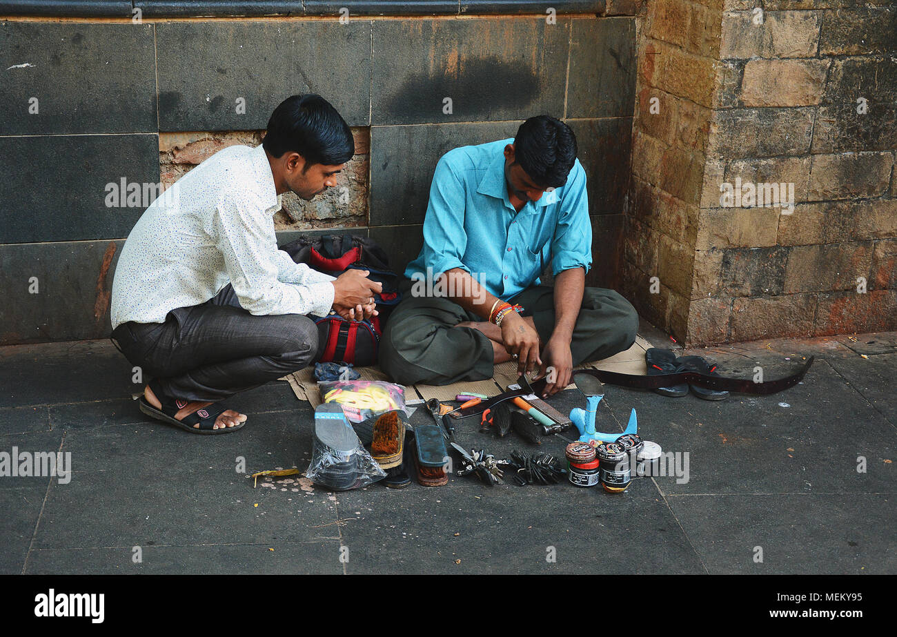 Una strada ciabattino lavorando come un cliente guarda, Mumbai, India Foto Stock